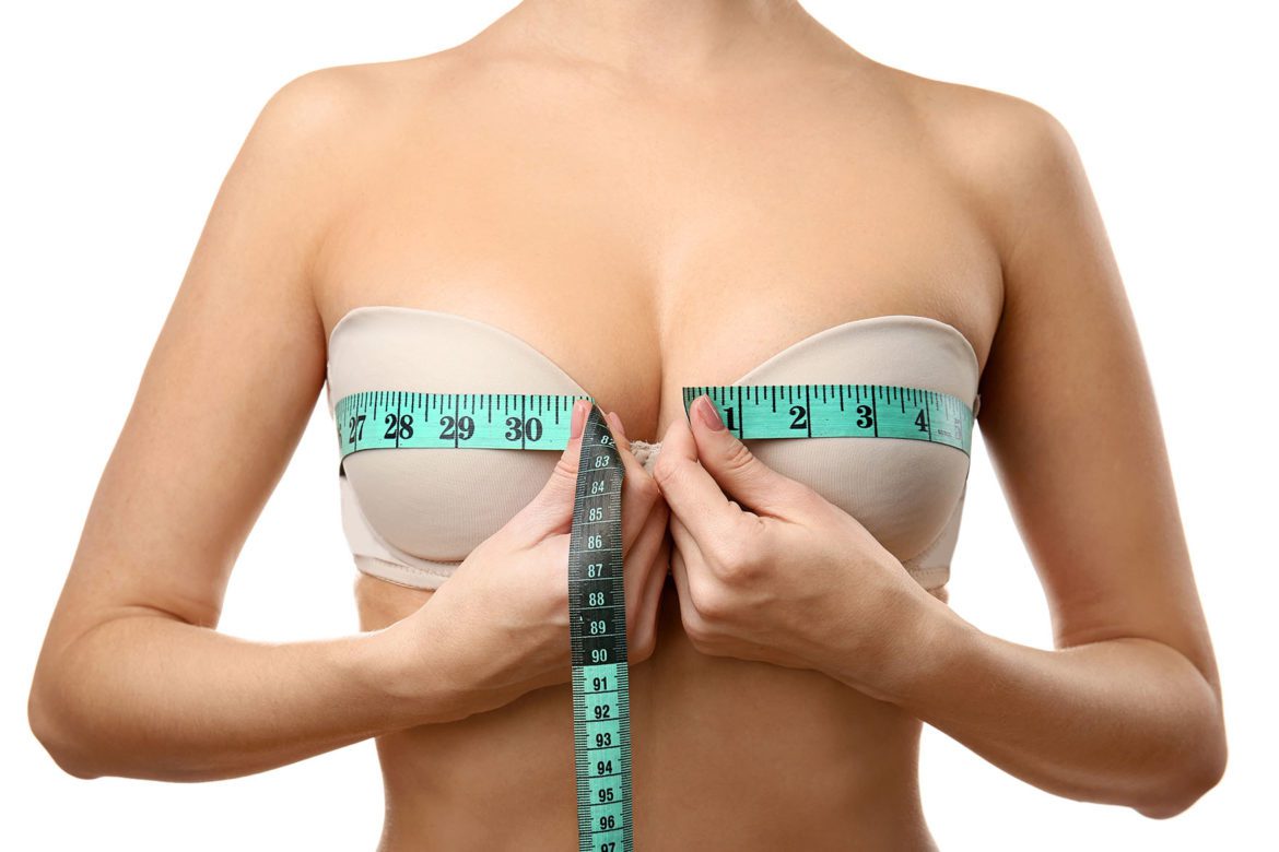 Young woman in beige bra with measuring tape on white background